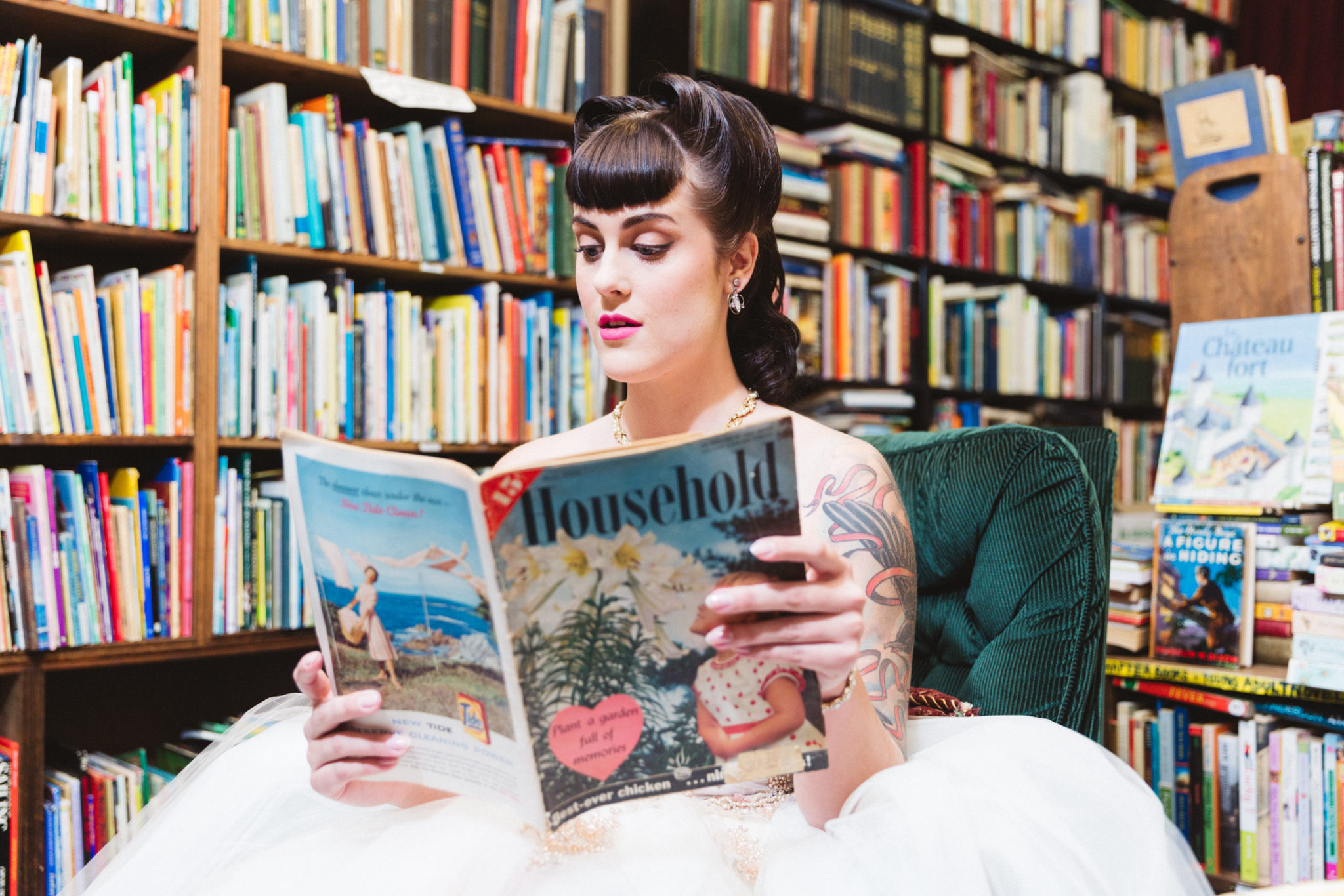 a bride in a 1950s styled shoot holding a copy of a magazine for housewives in owl and company vintage bookstore oakland