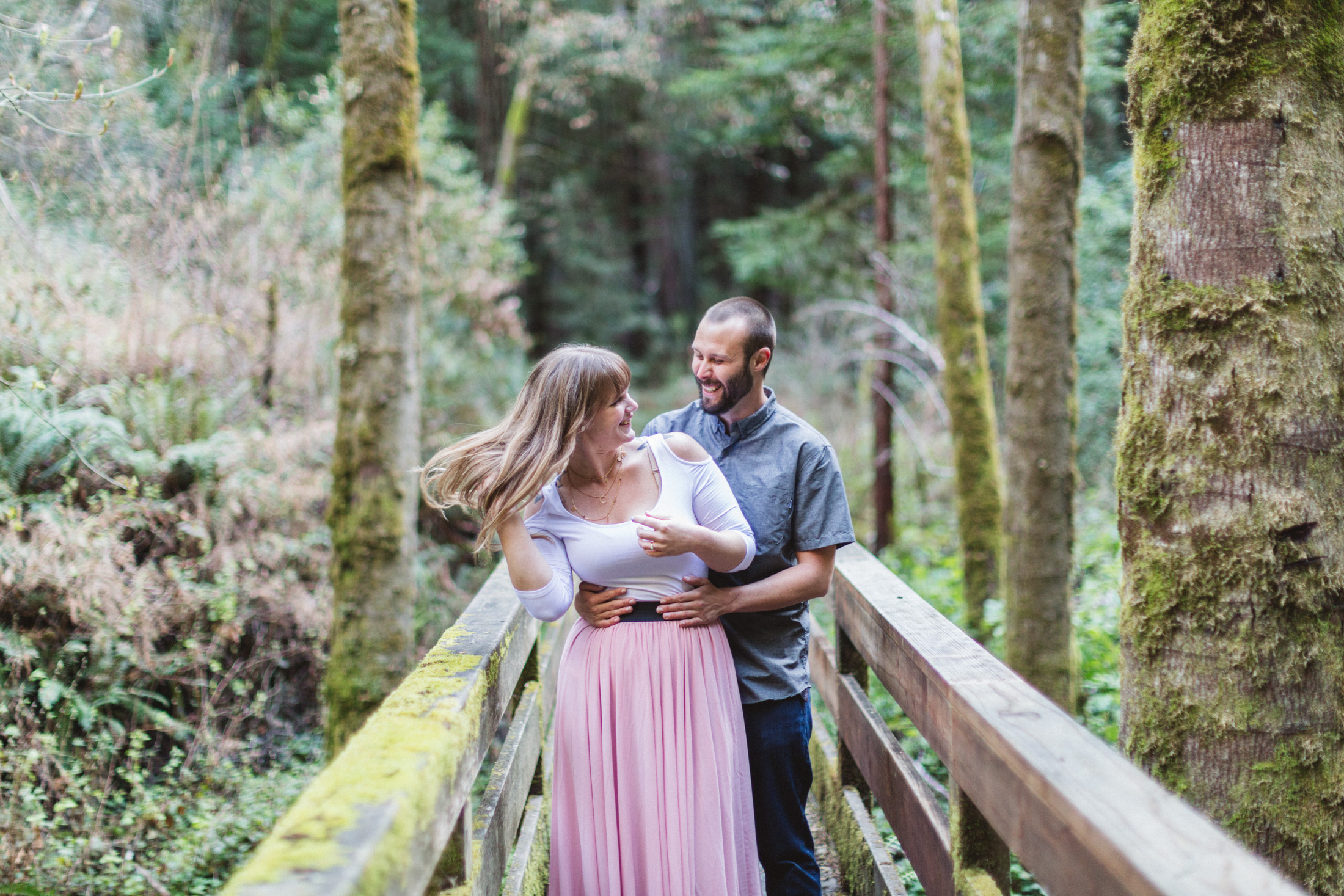 girl flicking hair on woodland bridge at engagement shoot