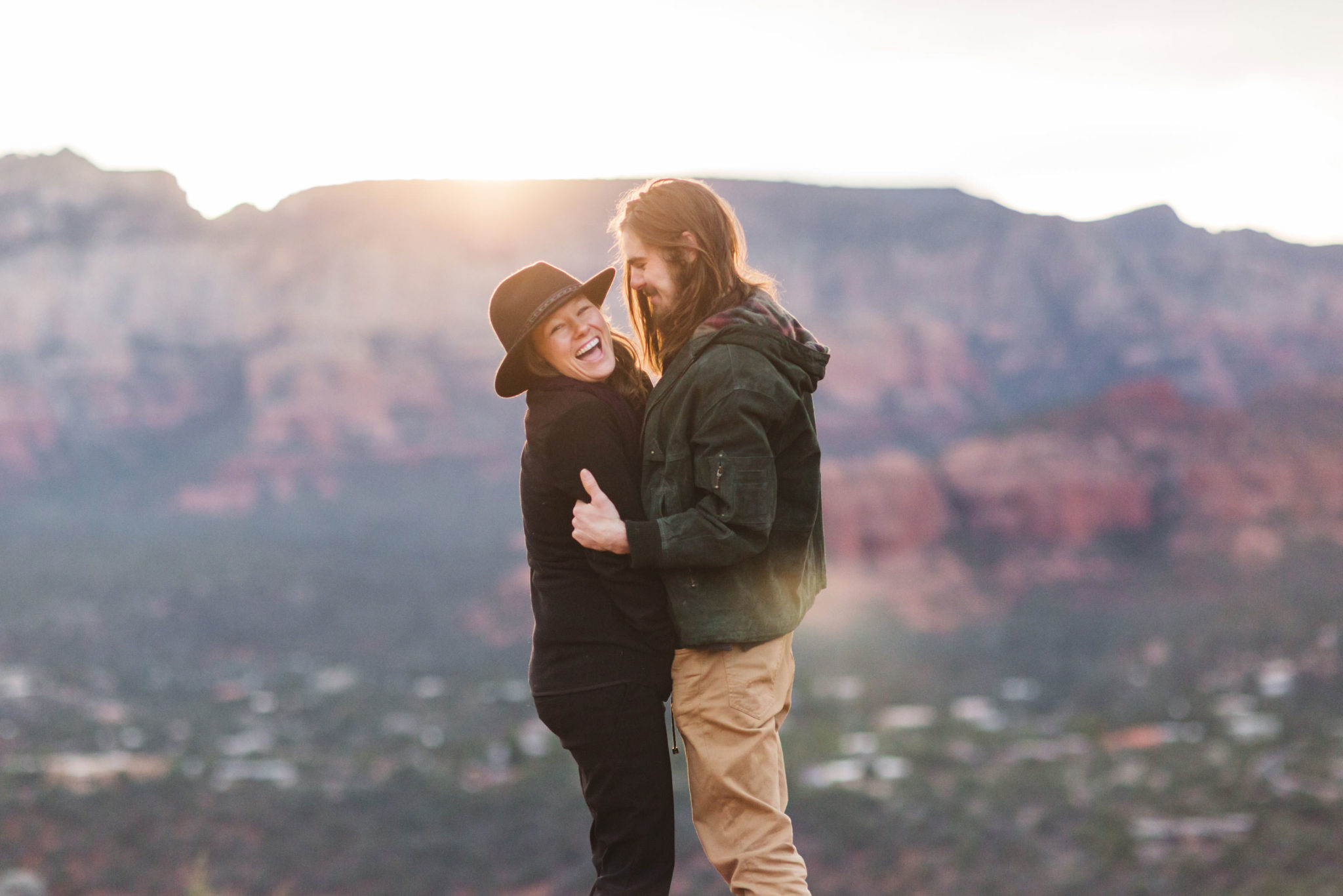 couple laughing with the red rocks of sedona behind them at sunrise